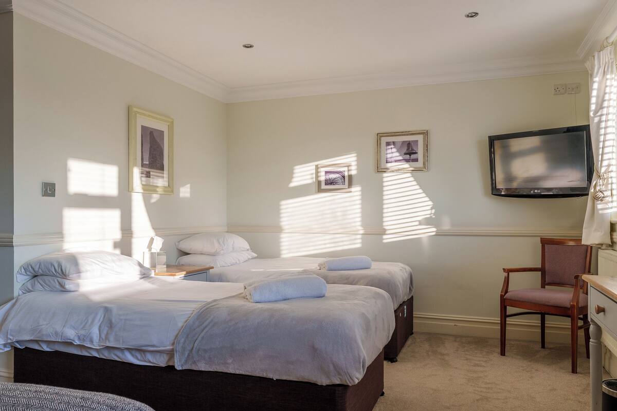 A hotel room with two beds, a TV mounted on the wall, and a desk with a chair.