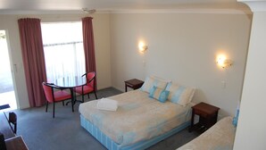 Ein Schlafzimmer mit einem Bett, einem Sessel, einem kleinen Tisch und einem Fenster mit Vorhängen.