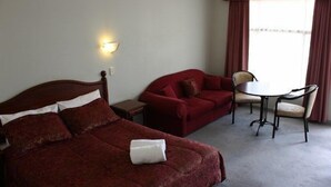 Ein Hotelzimmer mit einem Bett, einem roten Sofa, einem kleinen Tisch mit Stühlen und einem Fenster mit Vorhängen.