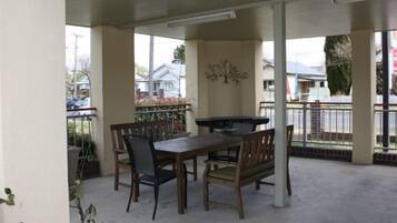 Un patio cubierto con una mesa y sillas de madera, una parrilla y vistas al barrio.