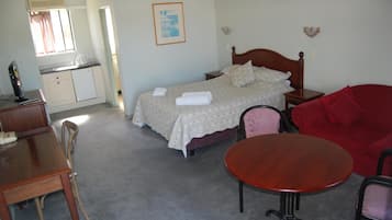Ein Schlafzimmer mit Bett, Nachttisch, einem kleinen Tisch, einem roten Sofa, einem Holzbüro mit Stühlen und einer Küchenzeile.