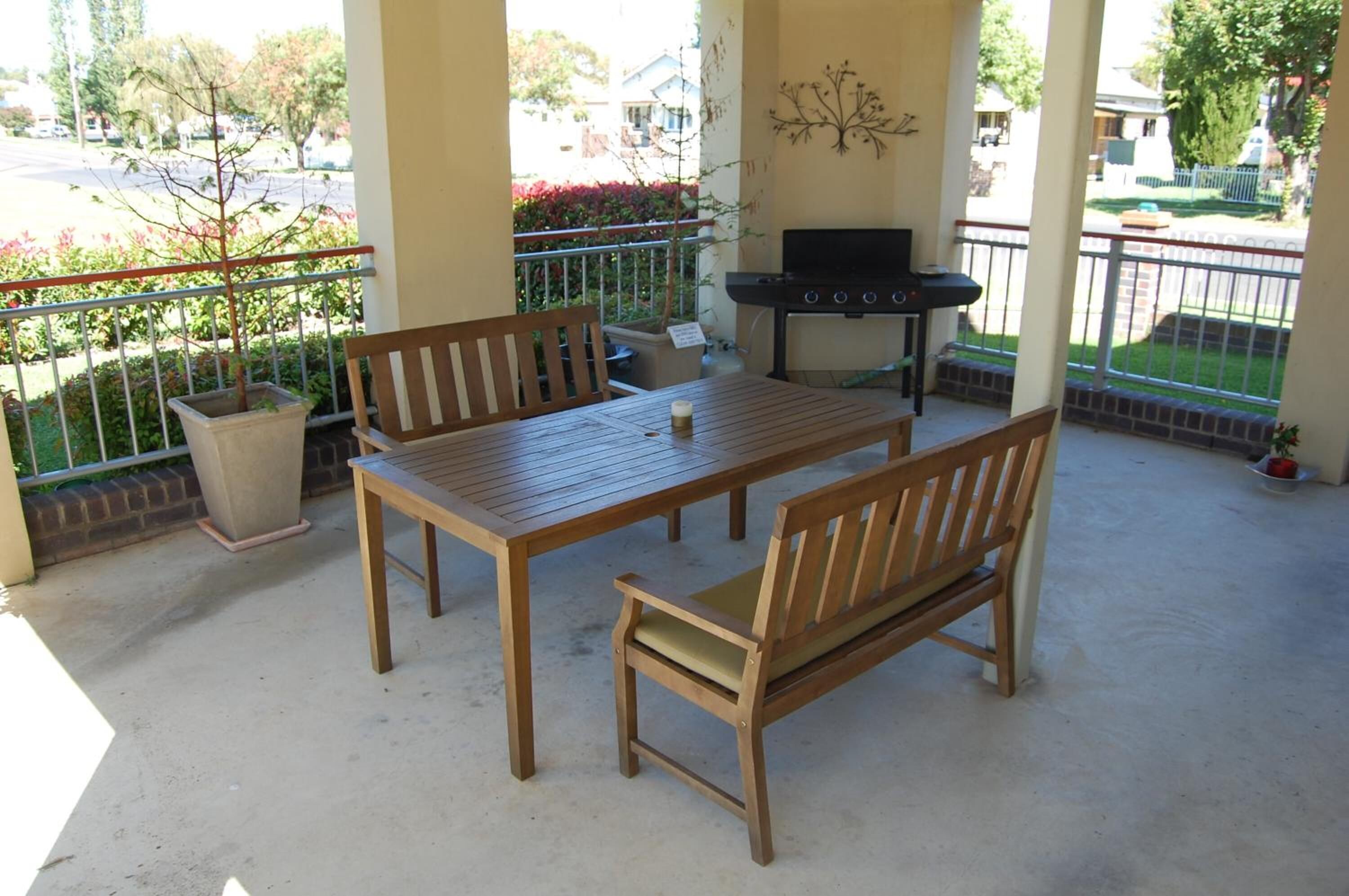 A covered patio area with a wooden table and benches, a grill, and potted plants.