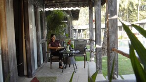 A covered outdoor seating area with a table and chairs, surrounded by wooden pillars and a glass door. - 19Belo Cabana (Calangute)