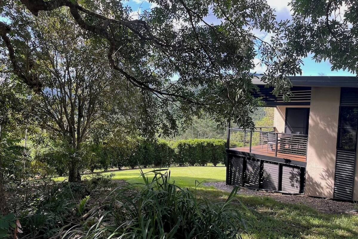 A modern building with a deck overlooking a well-maintained garden and a large tree.