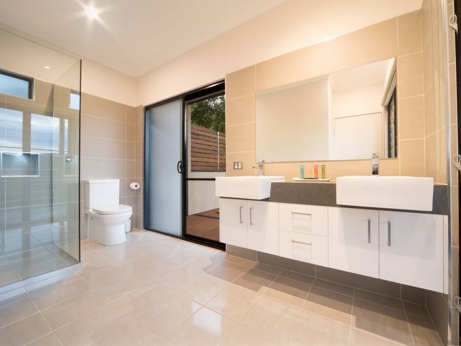 A modern bathroom with a glass shower enclosure, a toilet, and a double sink vanity with cabinets.
