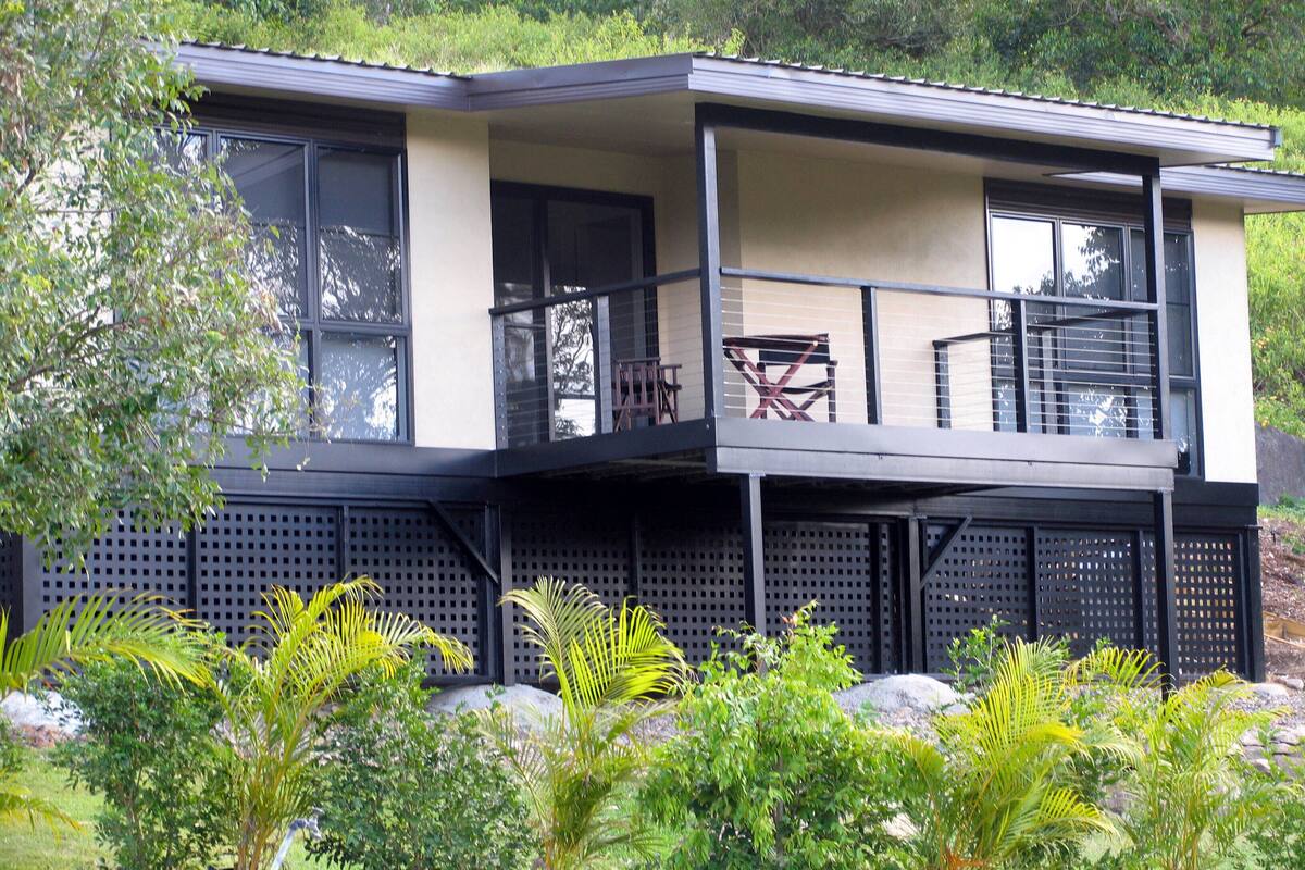 A two-story house with a balcony, large windows, and a surrounding garden.