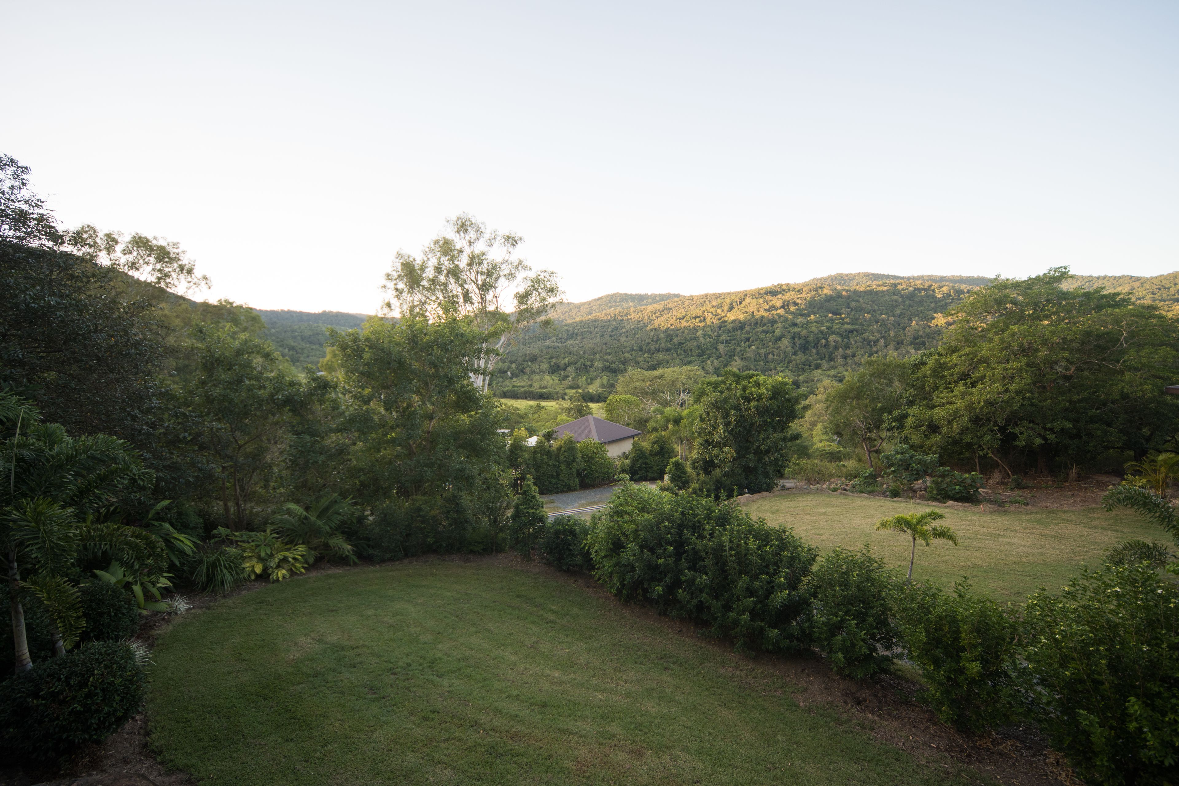 A residential area with a house surrounded by lush greenery and hills in the background.