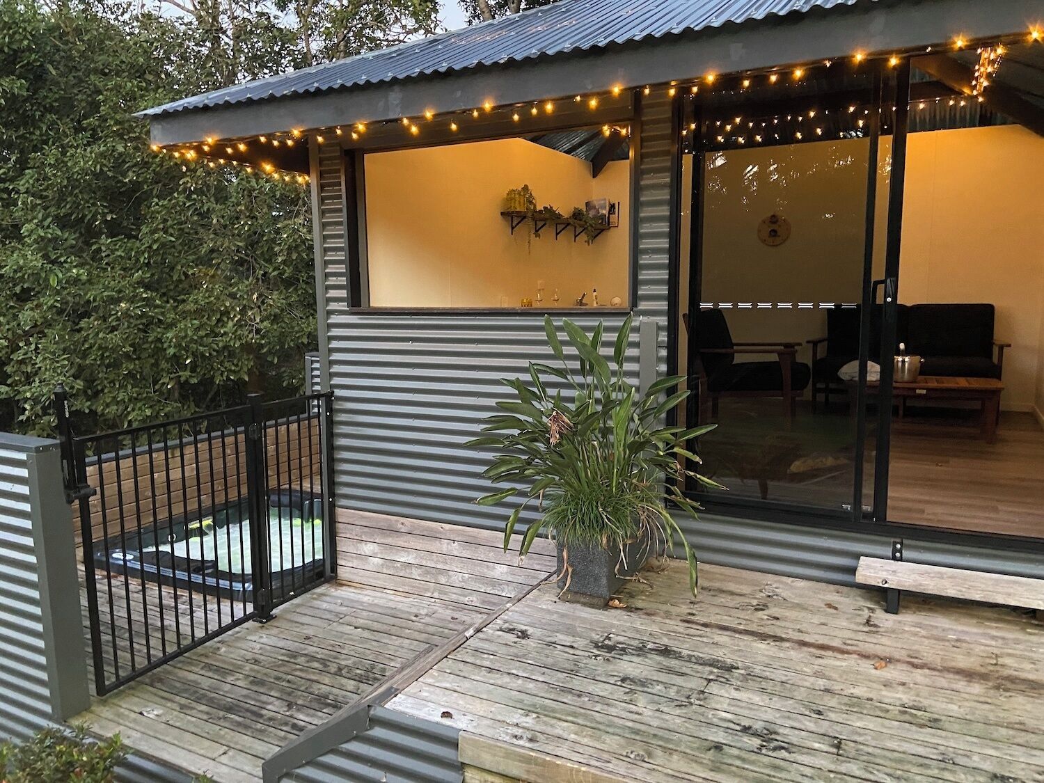 A modern outdoor deck with a metal railing, a potted plant, and string lights.