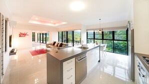 A modern kitchen with a large island, built-in appliances, and large windows offering a view of greenery.