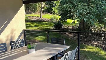 An outdoor patio with a table and chairs, a potted plant, and a view of a garden with trees and grass.