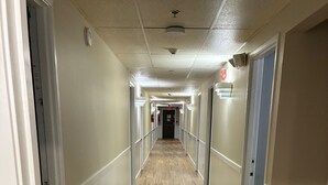 Un long couloir étroit, doté d’un plancher en bois et de murs blancs, qui mène à une porte au bout.