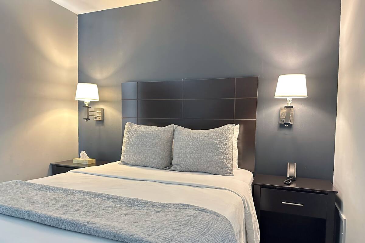 A neatly made bed with a grey quilt, two bedside lamps, and a dark headboard.