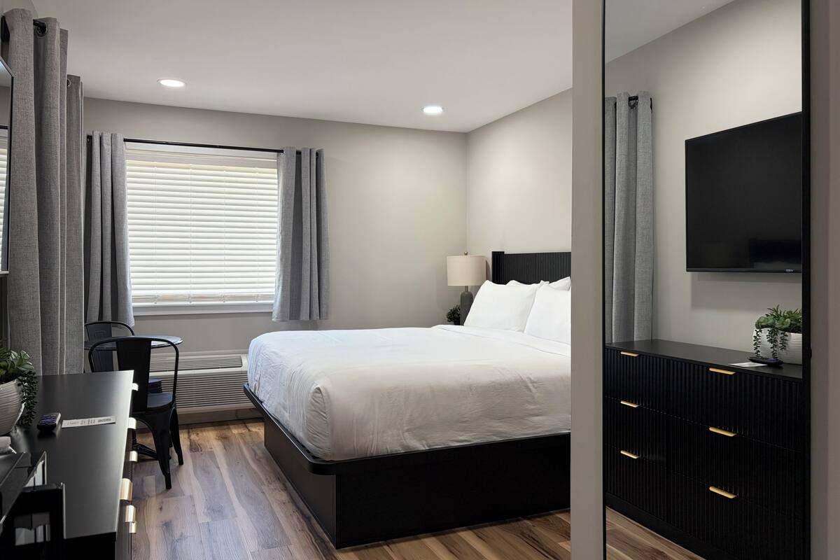 A modern hotel room with a bed, desk, chair, and a TV.