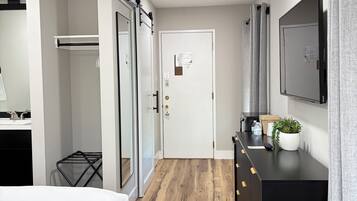 A hotel room with a bed, a dresser, a mirror, a door, and a small plant.