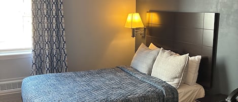Een hotelkamer met een bed, nachtkastje, lamp en uitzicht op het omliggende landschap.