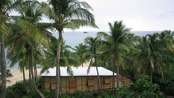 A beach house with a white roof, surrounded by palm trees and overlooking the ocean.