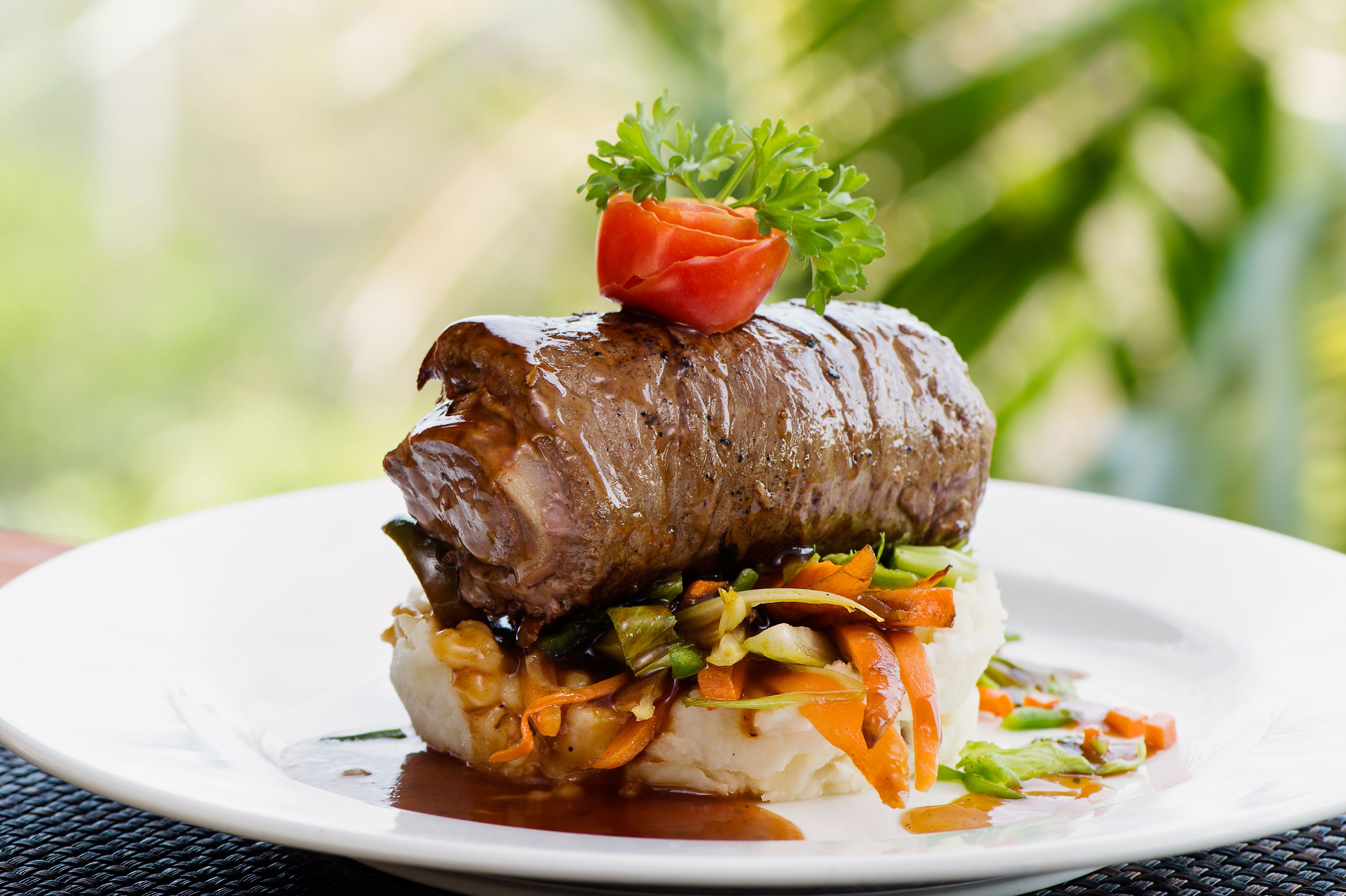 Un plat composé d’un rouleau de bœuf, de légumes et d’une garniture, le tout présenté sur une assiette blanche.