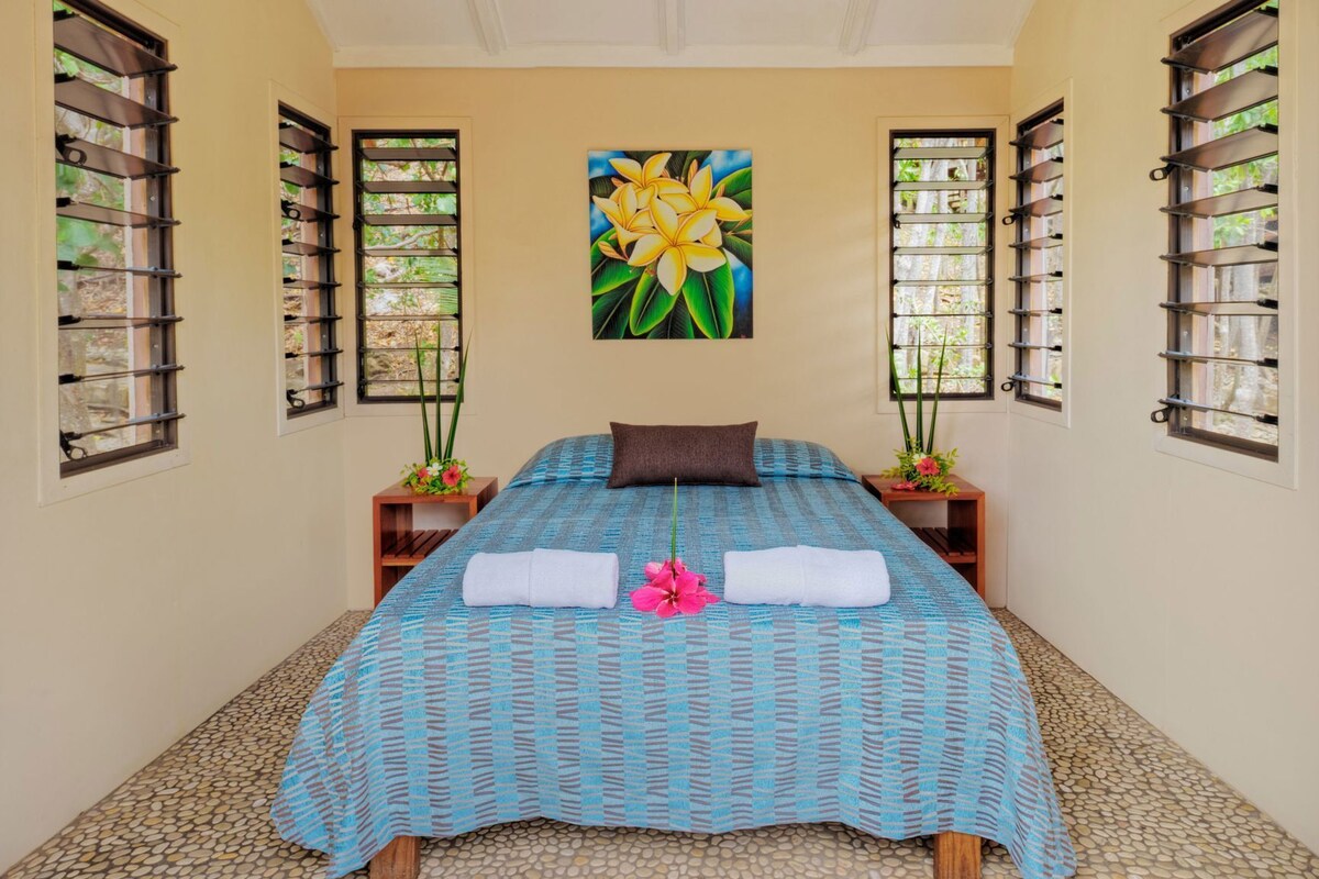 A room with a bed, two nightstands, a painting, and windows with blinds.