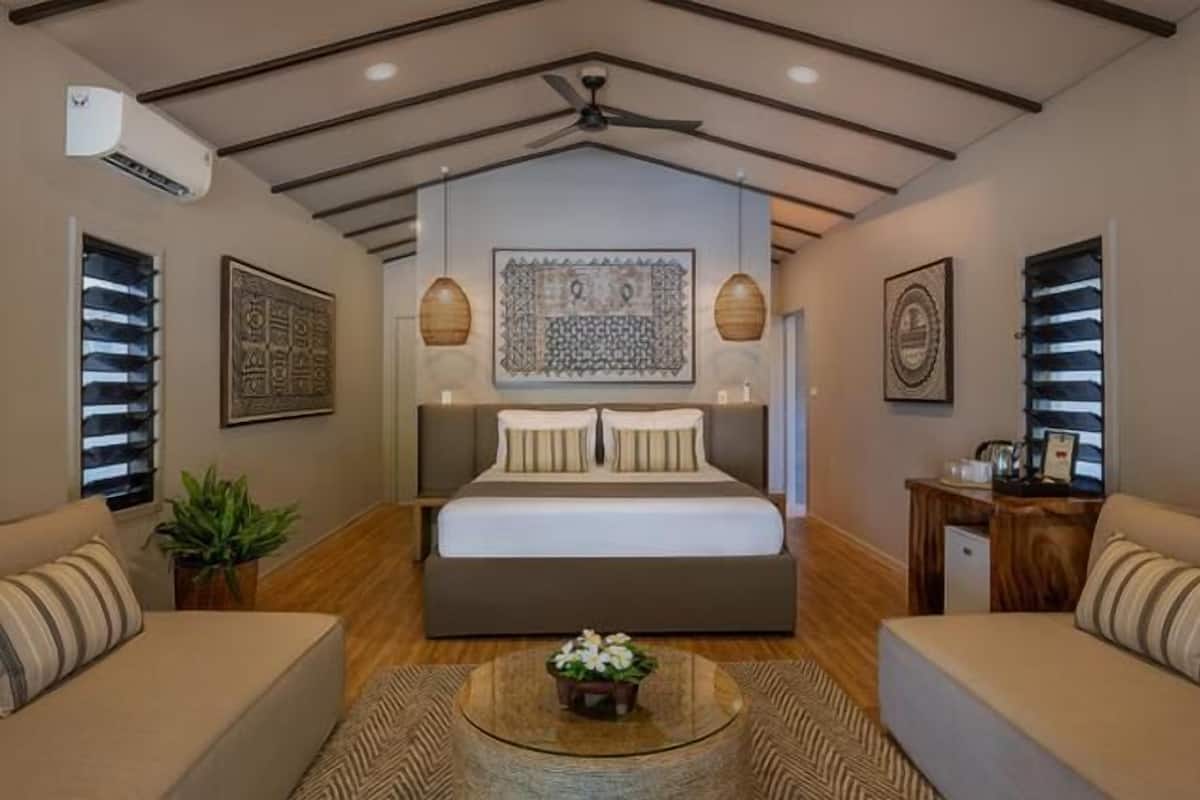 Een slaapkamer met een groot bed, twee nachtkastjes, een plafondventilator en decoratieve wandkunst.