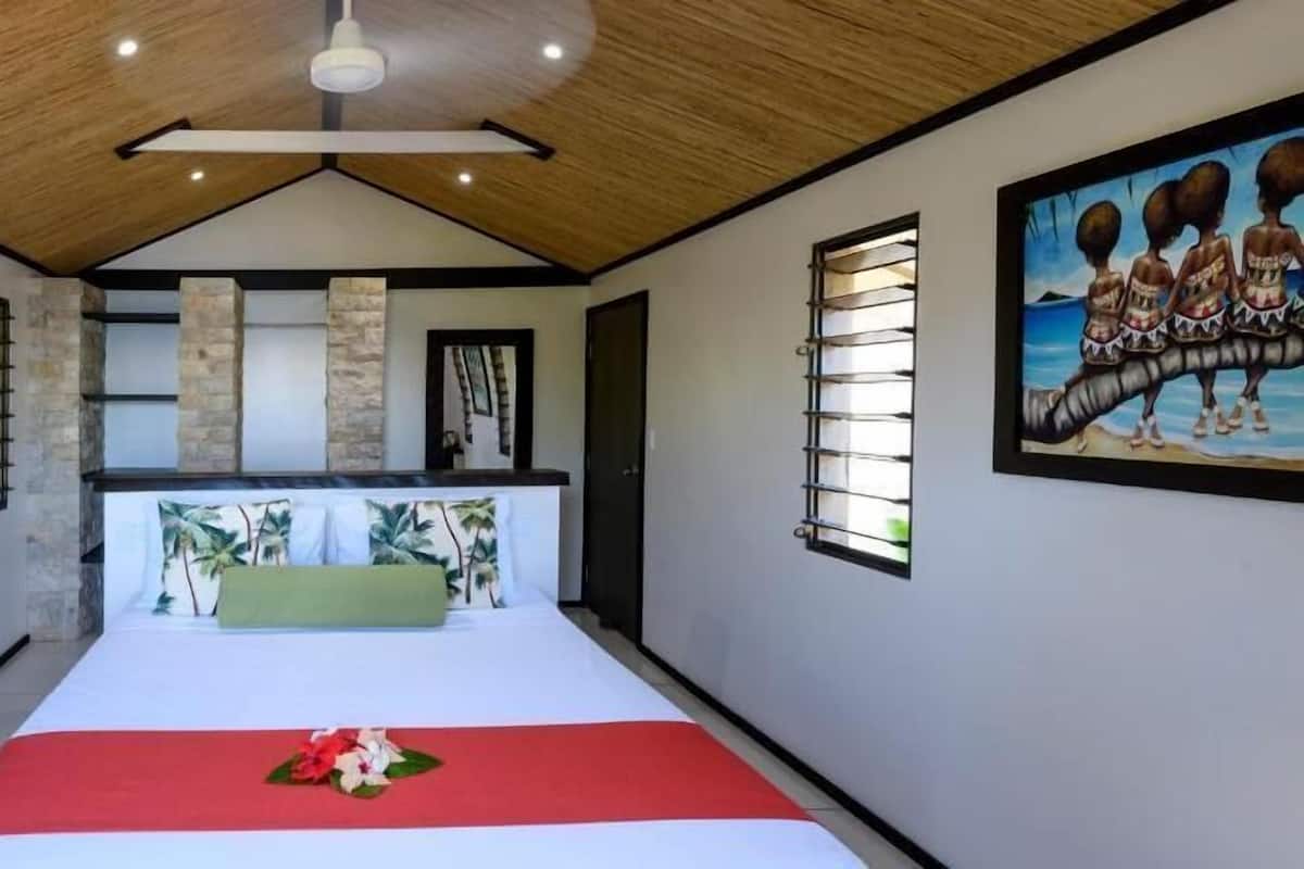 Een slaapkamer met een bed, een schilderij en een plafondventilator.