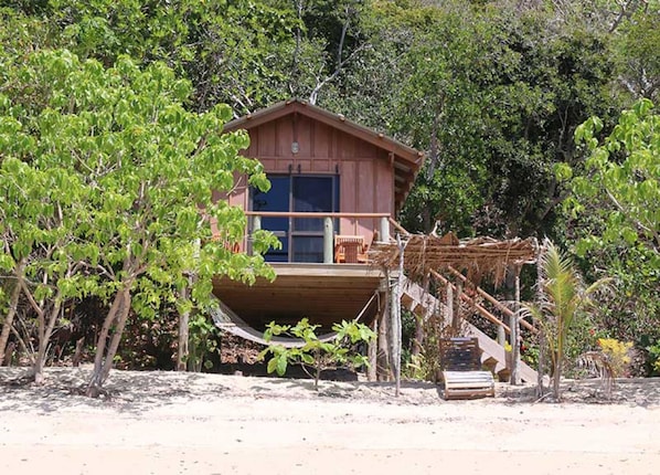 Una cabaña de madera con balcón, rodeada de árboles y vegetación.