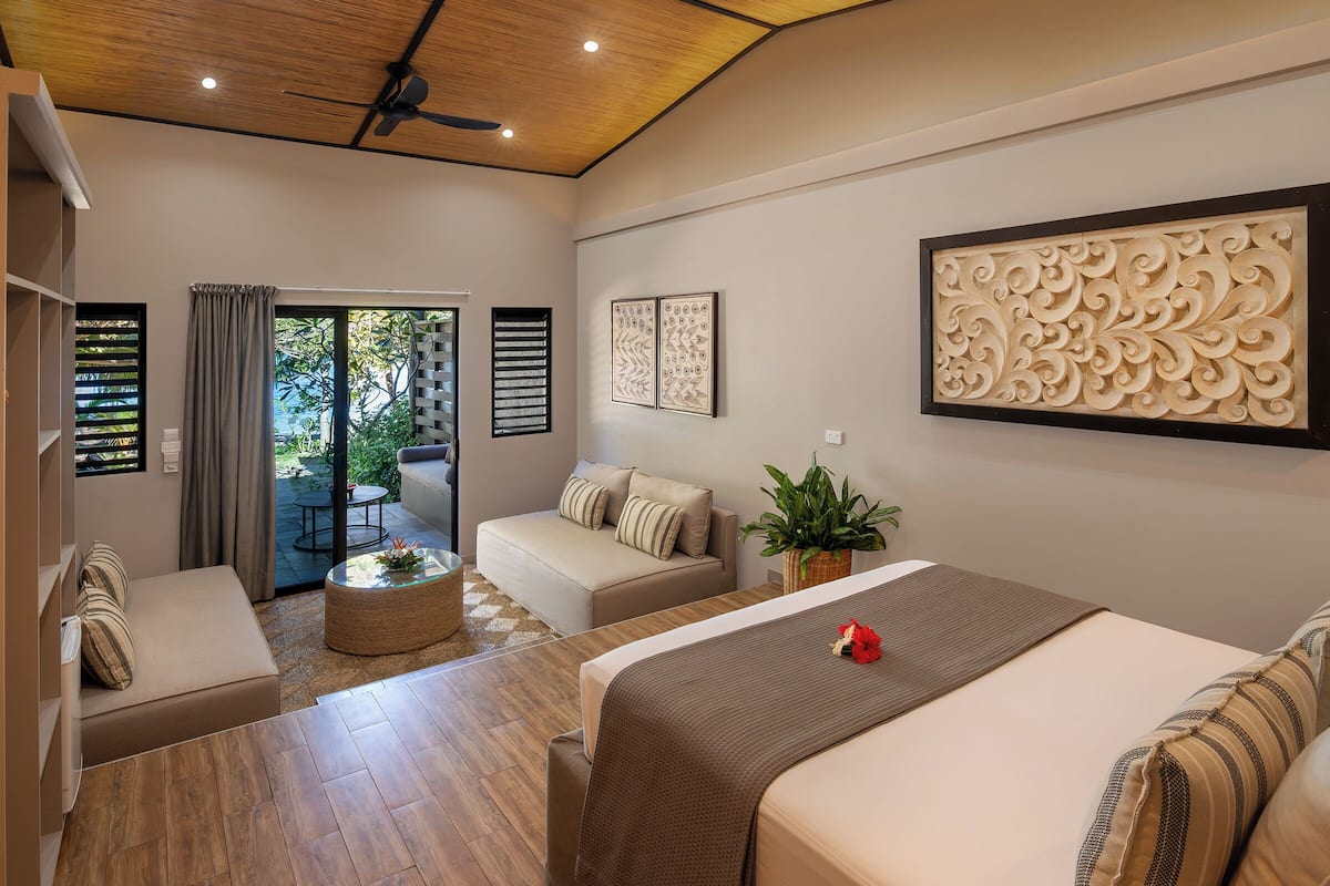 Een moderne hotelkamer met een bed, een sofa, een bijzettafeltje en een balkon met uitzicht op groen.