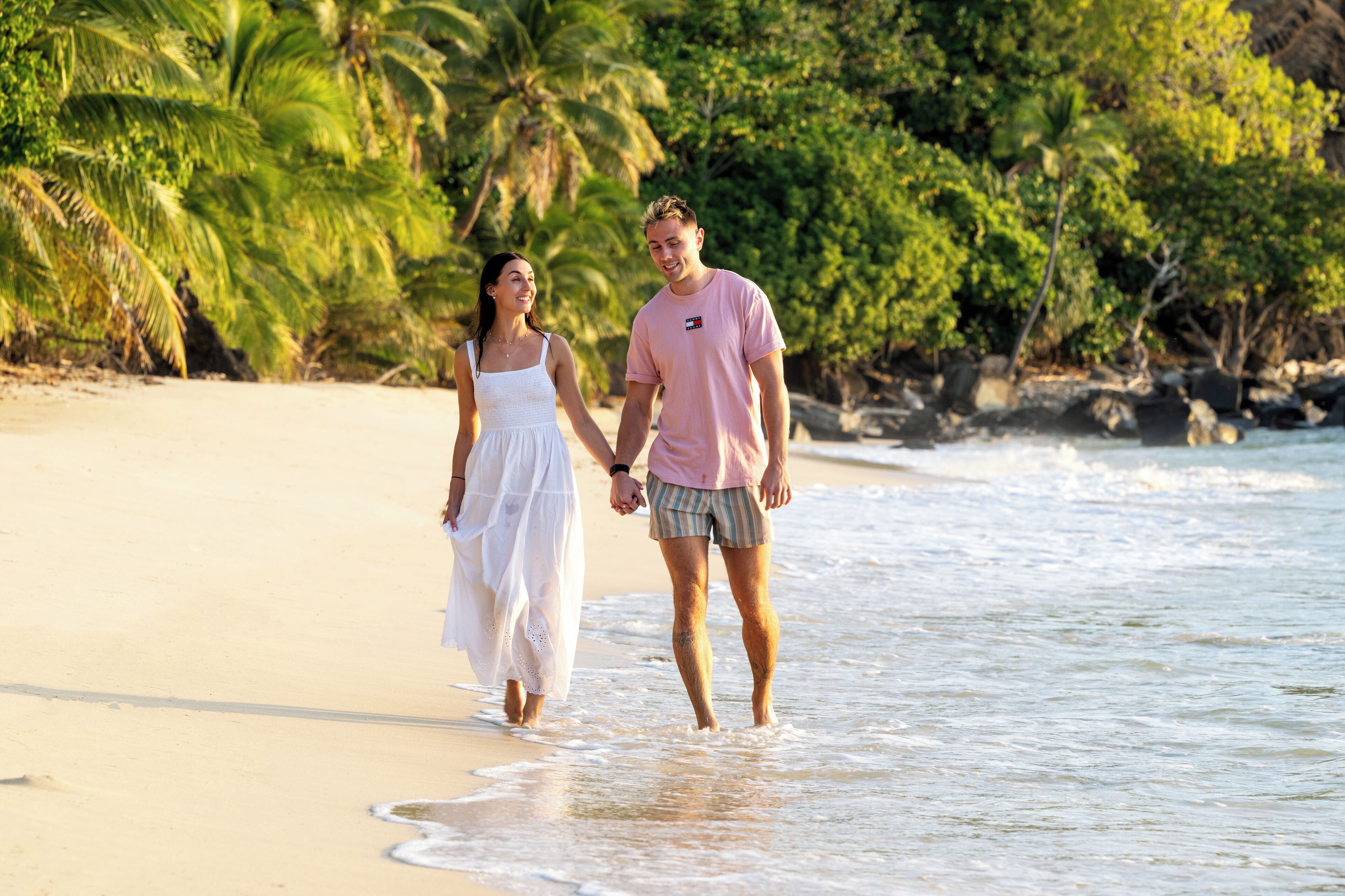 A couple walking on a beach with palm trees and ocean in the background.