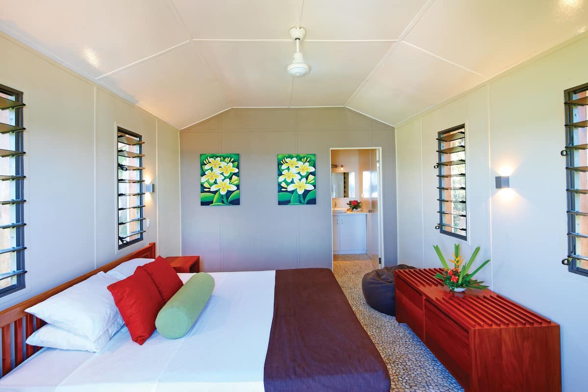 Een slaapkamer met een bed, kussens, een bankje en kunstwerken aan de muren.