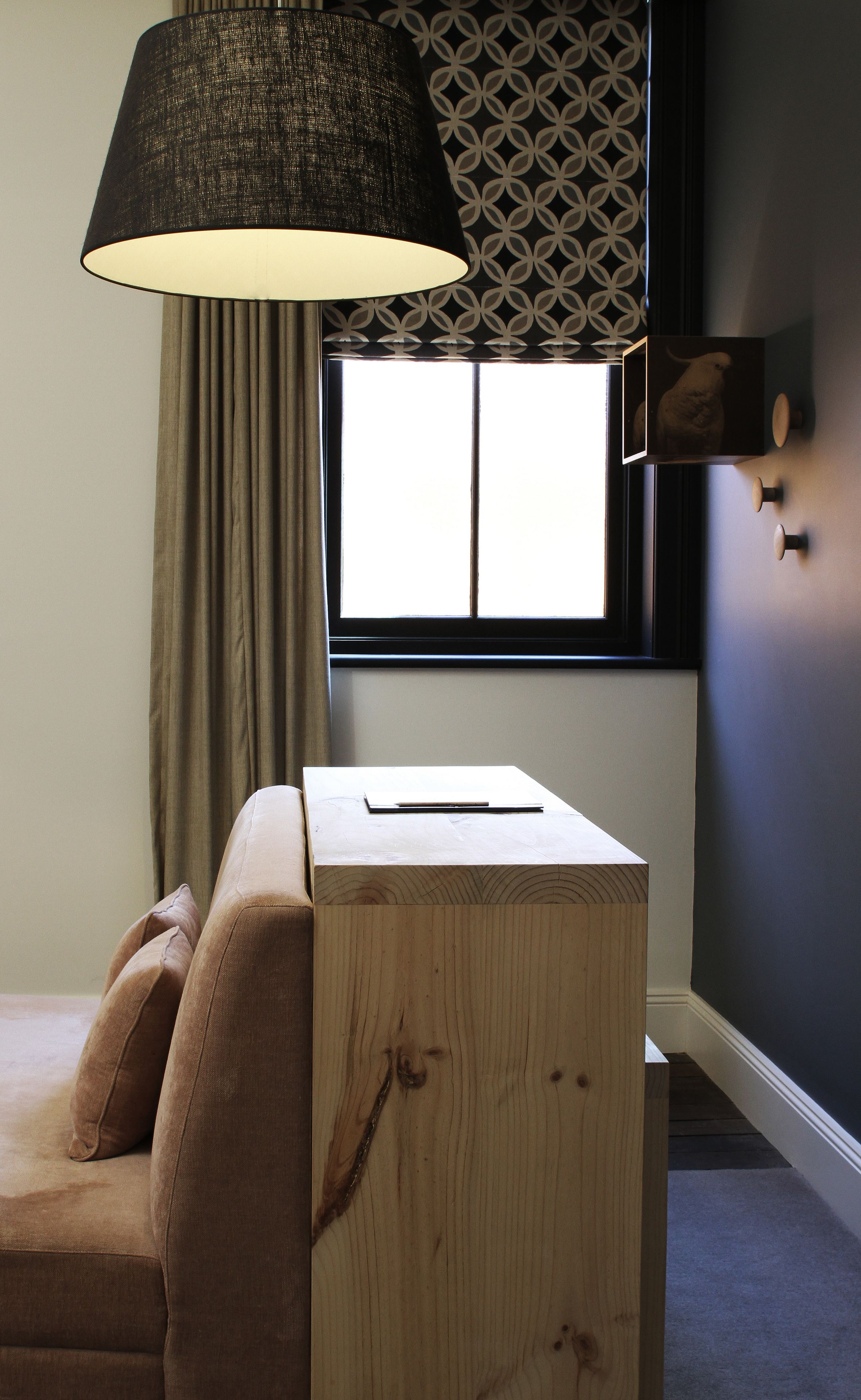 A room with a wooden desk, a lamp, a window with a view, and a patterned wall.