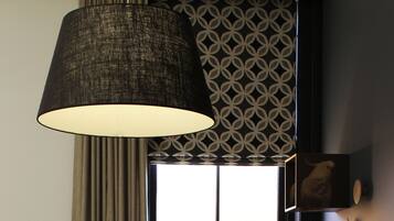 A room with a wooden desk, a lamp, a window with a view, and a patterned wall.