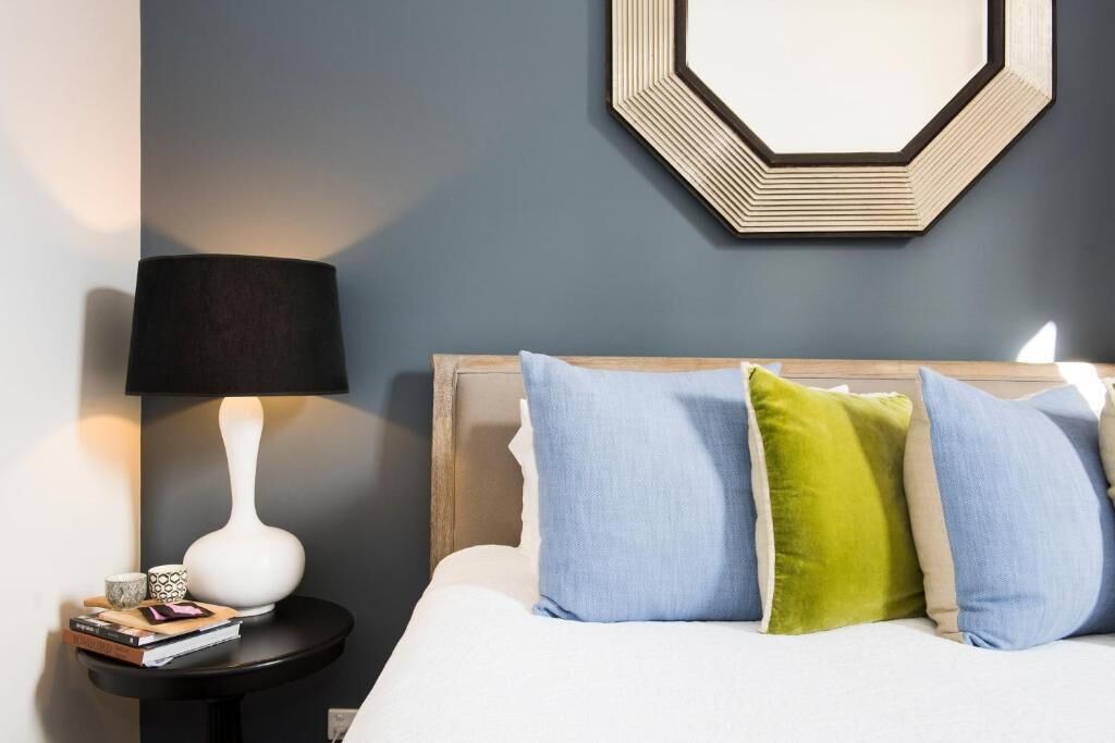 A neatly made bed with a wooden headboard, a bedside lamp, and a small table with books and a decorative item.
