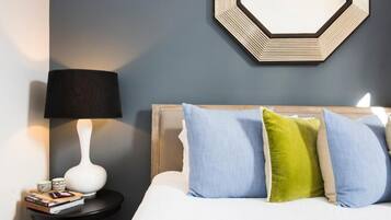 A neatly made bed with a wooden headboard, a bedside lamp, and a small table with books and a decorative item.