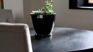 Una mesa redonda con una planta en maceta en el centro, una silla en primer plano y una ventana al fondo.