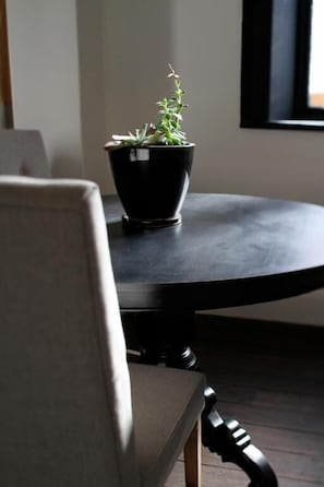 A round table with a potted plant in the center, a chair in the foreground, and a window in the background.