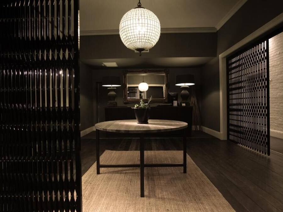 A dimly lit room with a round table, two lamps, a potted plant, and a decorative wall panel.