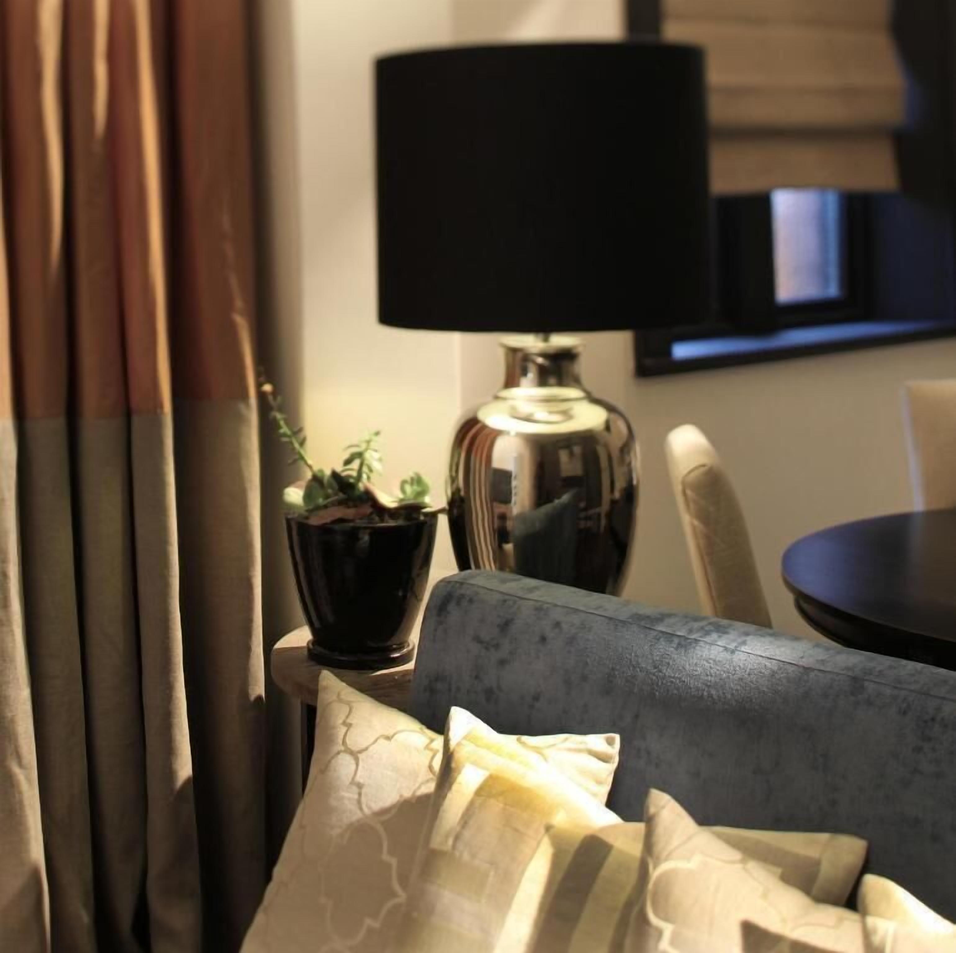 A room with a sofa, a black lamp, a potted plant, and a window with curtains.