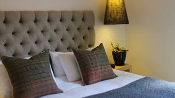 A neatly made bed with a tufted headboard, two plaid pillows, and a bedside table with a lamp and a potted plant.