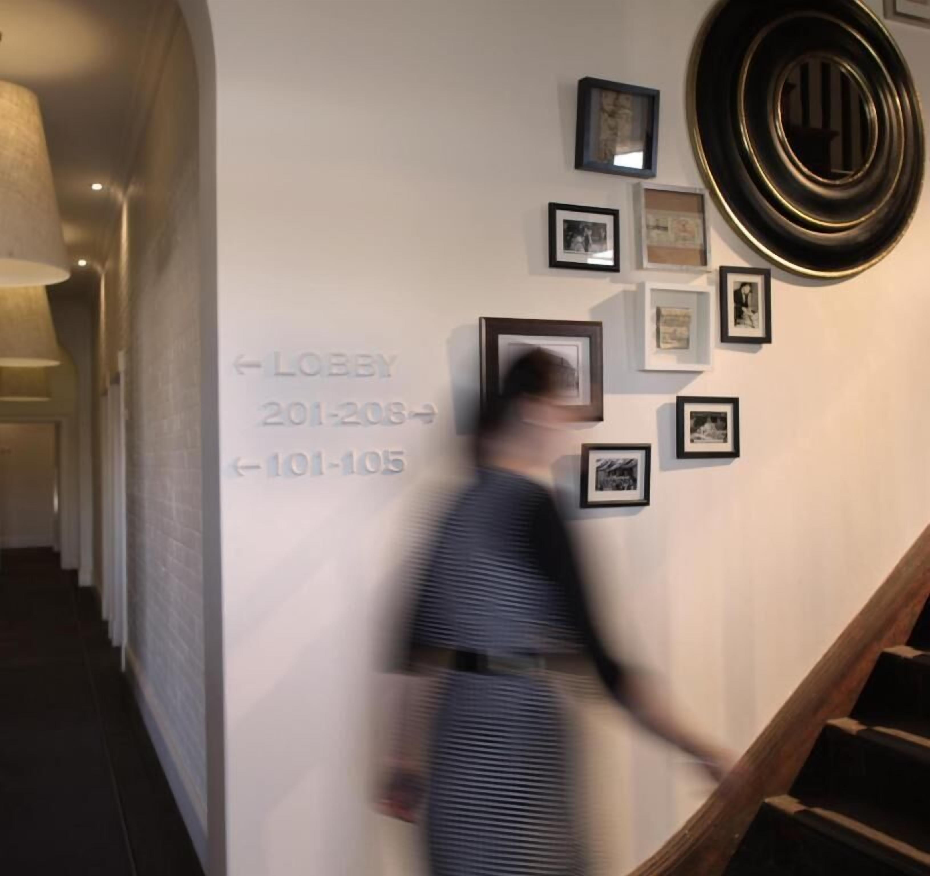 A hallway with a staircase, a wall with framed pictures, and directional signs for the lobby.