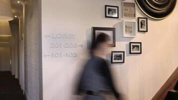 A hallway with a staircase, a wall with framed pictures, and directional signs for the lobby.