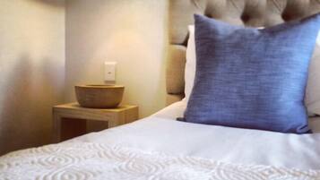 A neatly made bed with a tufted headboard, a small bedside table with a bowl, and a lamp.