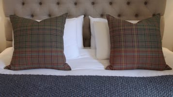 A bed with a tufted headboard, two plaid pillows, and white pillows.