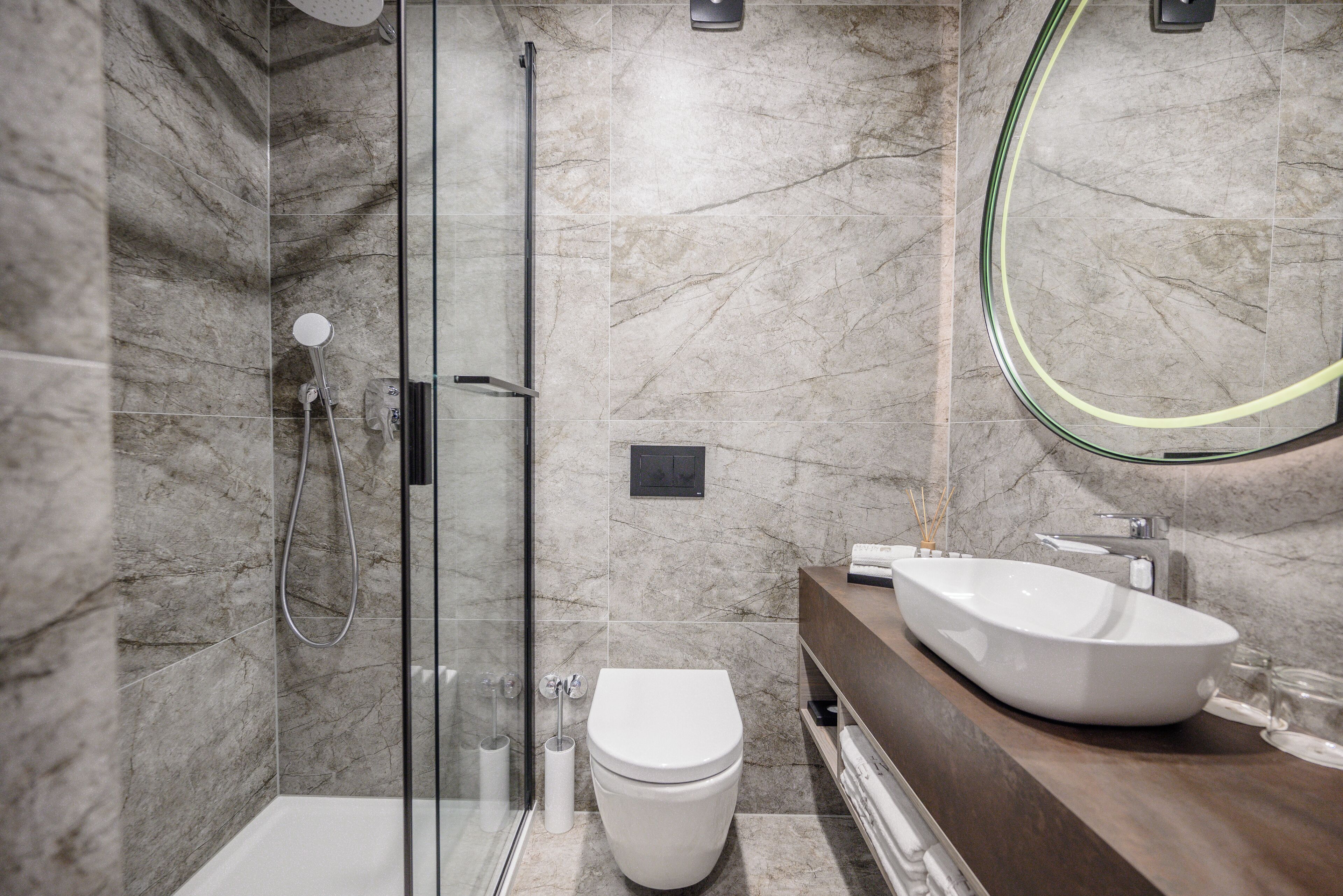 Une salle de bain moderne avec une douche à parois de verre, des toilettes blanches et un grand lavabo ovale doté d’un plan de travail en bois.