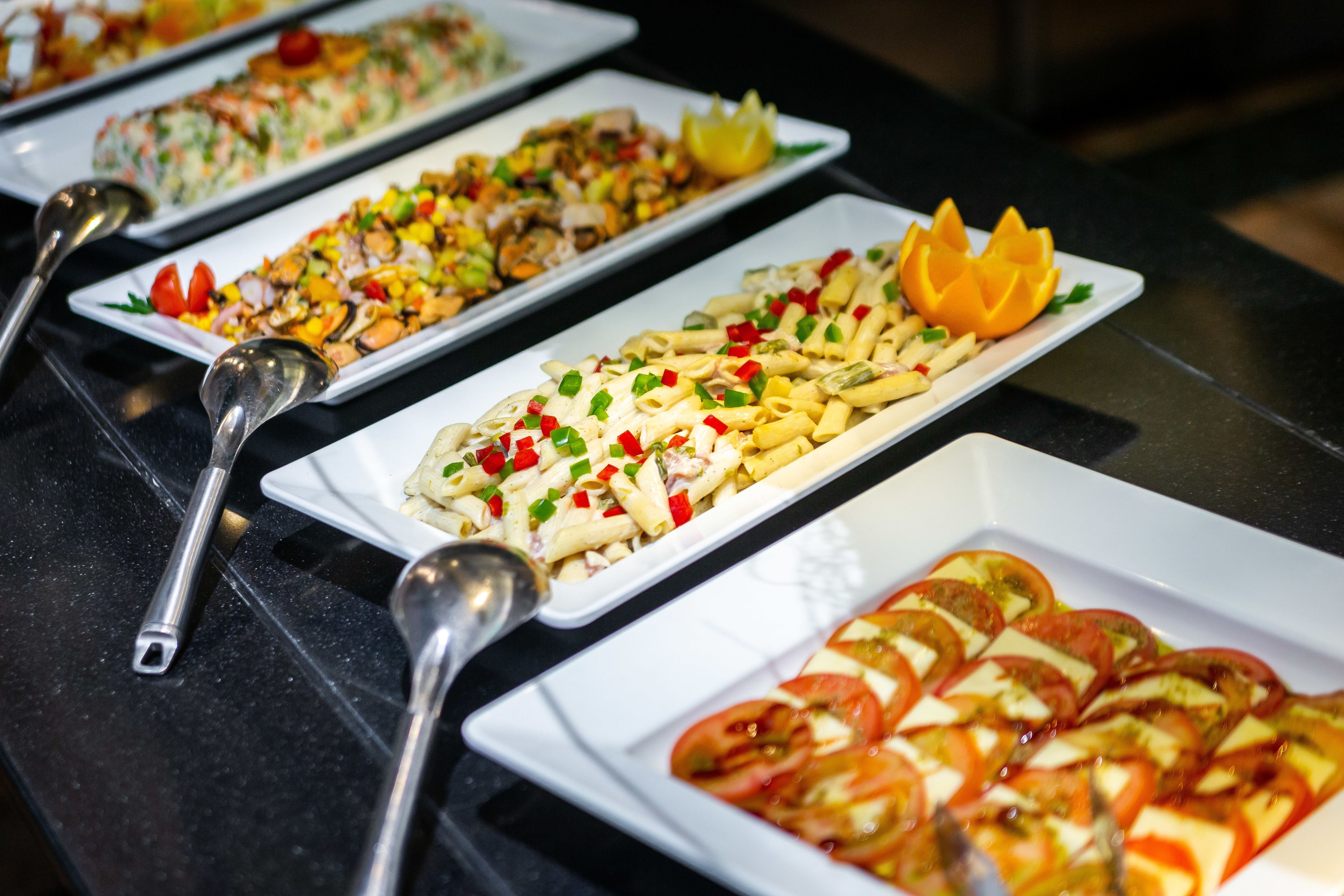 En buffet med forskellige retter, blandt andet pasta, salater og frugtpynt.