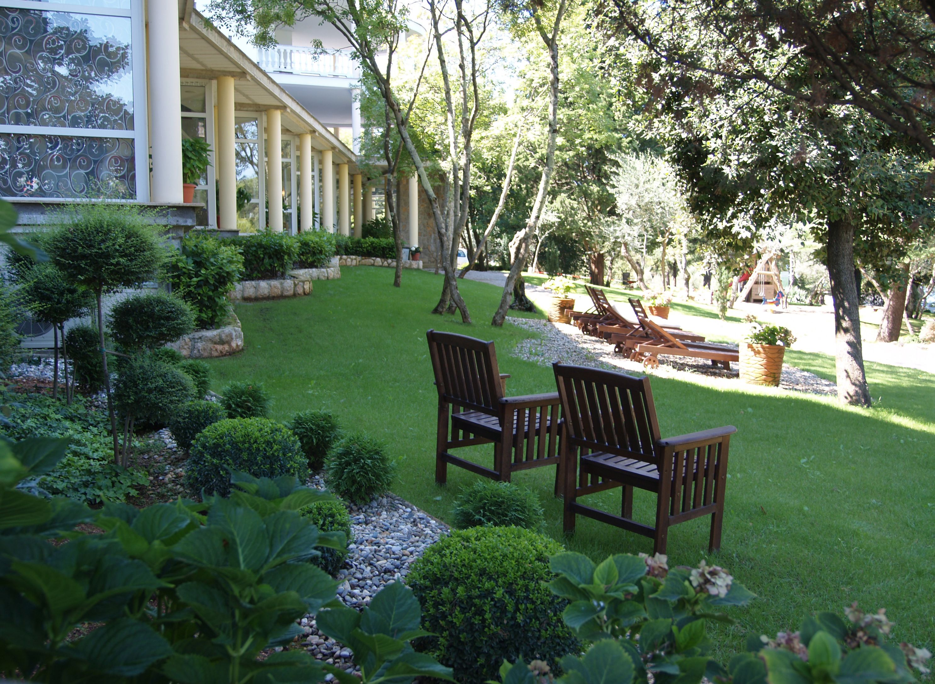 A well-maintained garden with a lawn, two wooden chairs, and a stone pathway.