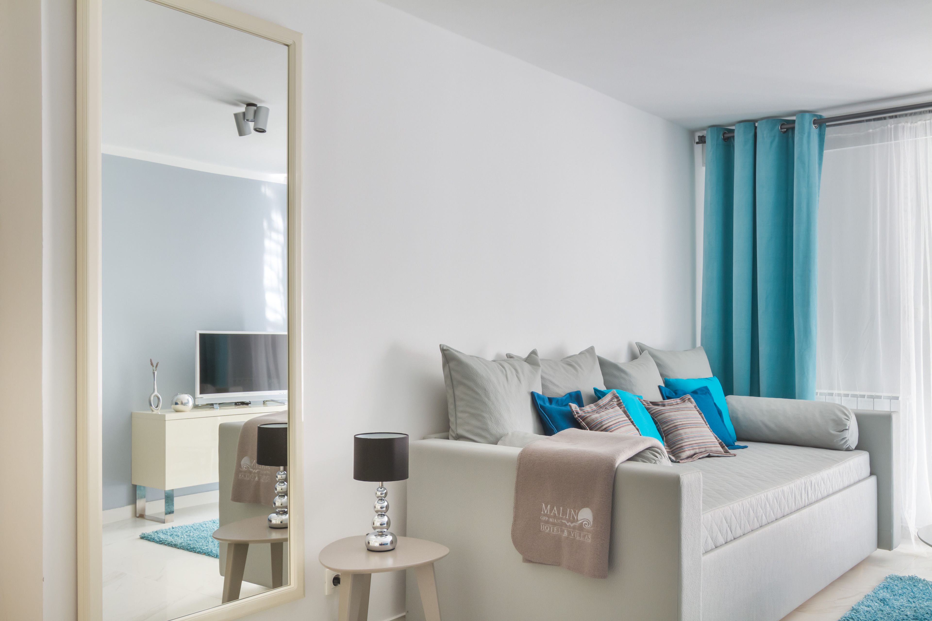 Une chambre d’hôtel moderne équipée d’un lit, d’une télévision, d’une petite table avec une lampe et d’un miroir.