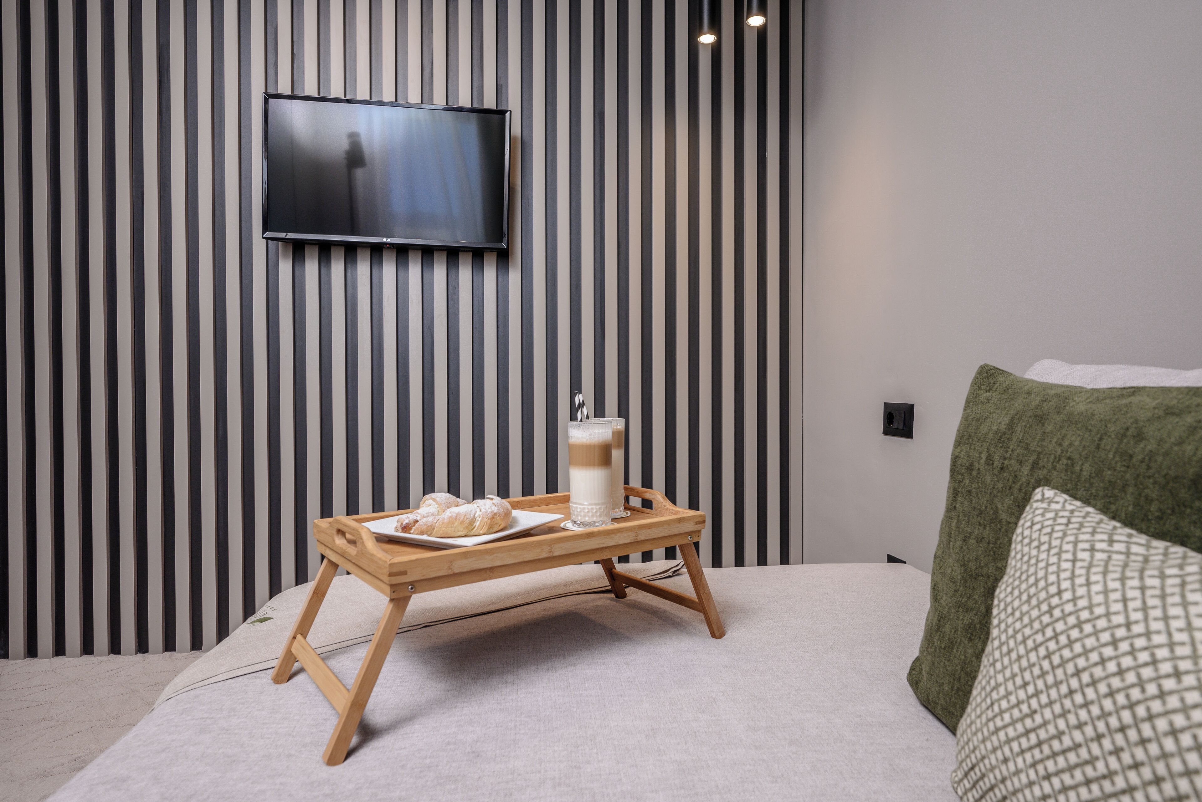 A modern room with a bed, a tray with pastries and a glass of milk, a television on the wall, and a striped wallpaper pattern.
