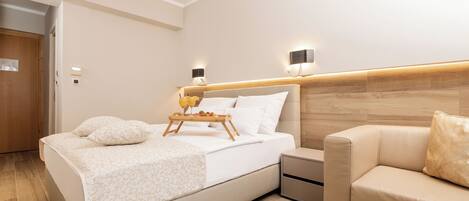 Una habitación de hotel moderna con una cama grande, mesitas de noche, un sofá y un cabecero de madera.