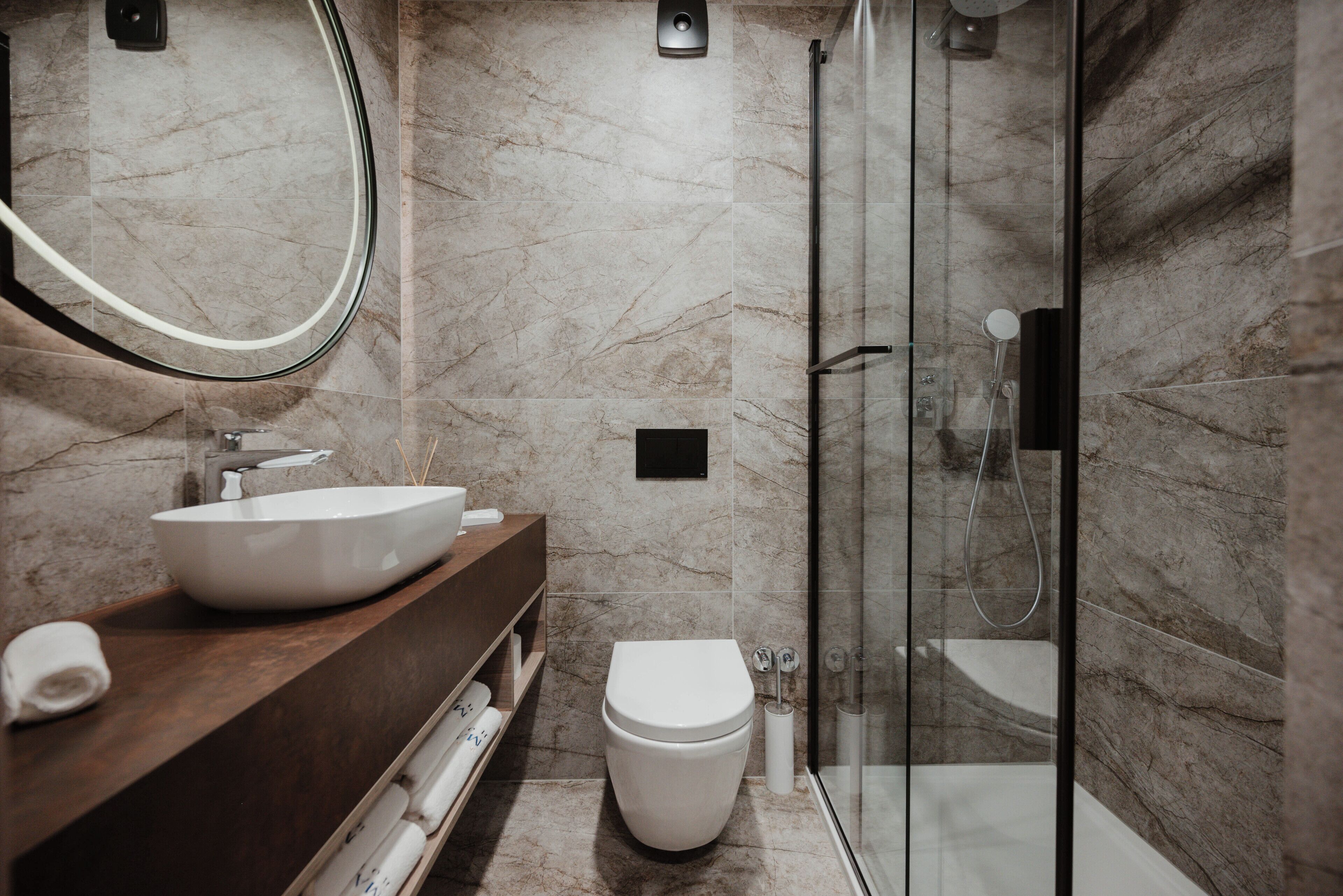 A modern bathroom with a marble floor, a white sink, a toilet, and a glass-enclosed shower area.
