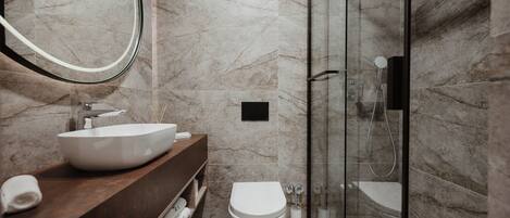A modern bathroom with a marble floor, a white sink, a toilet, and a glass-enclosed shower area.