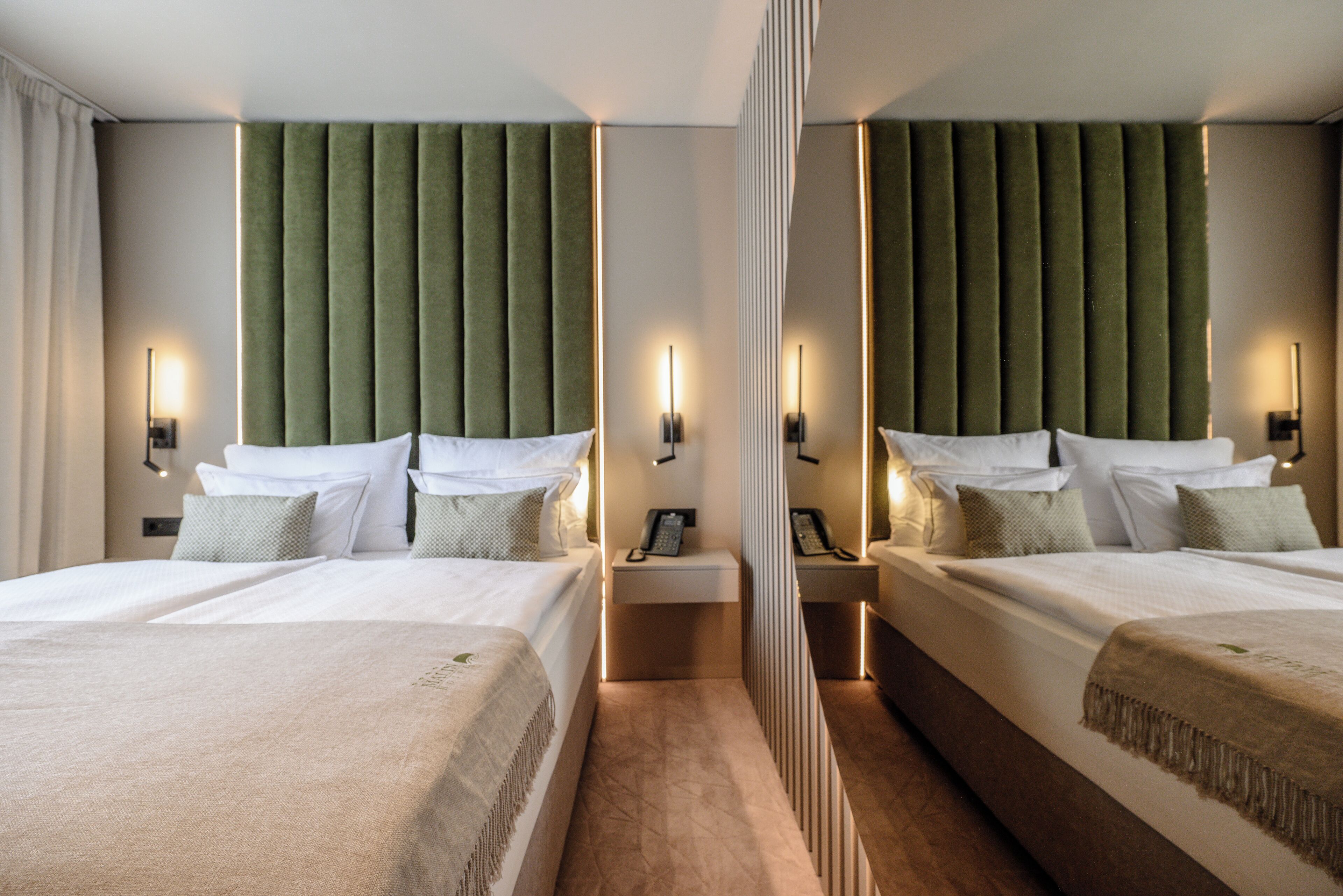 Habitación de hotel con dos camas, un espejo y una mesita de noche con teléfono.